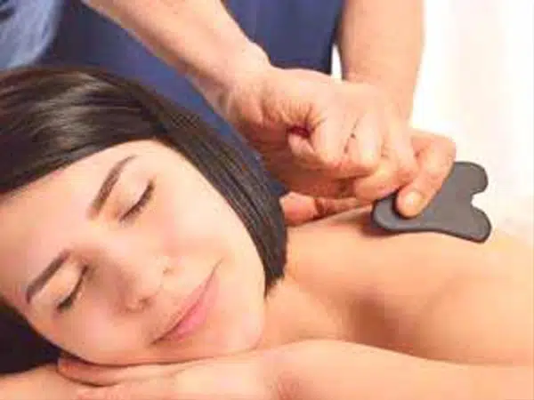 Body gua sha. A practitioner is using a stone tool to scrape patient's back